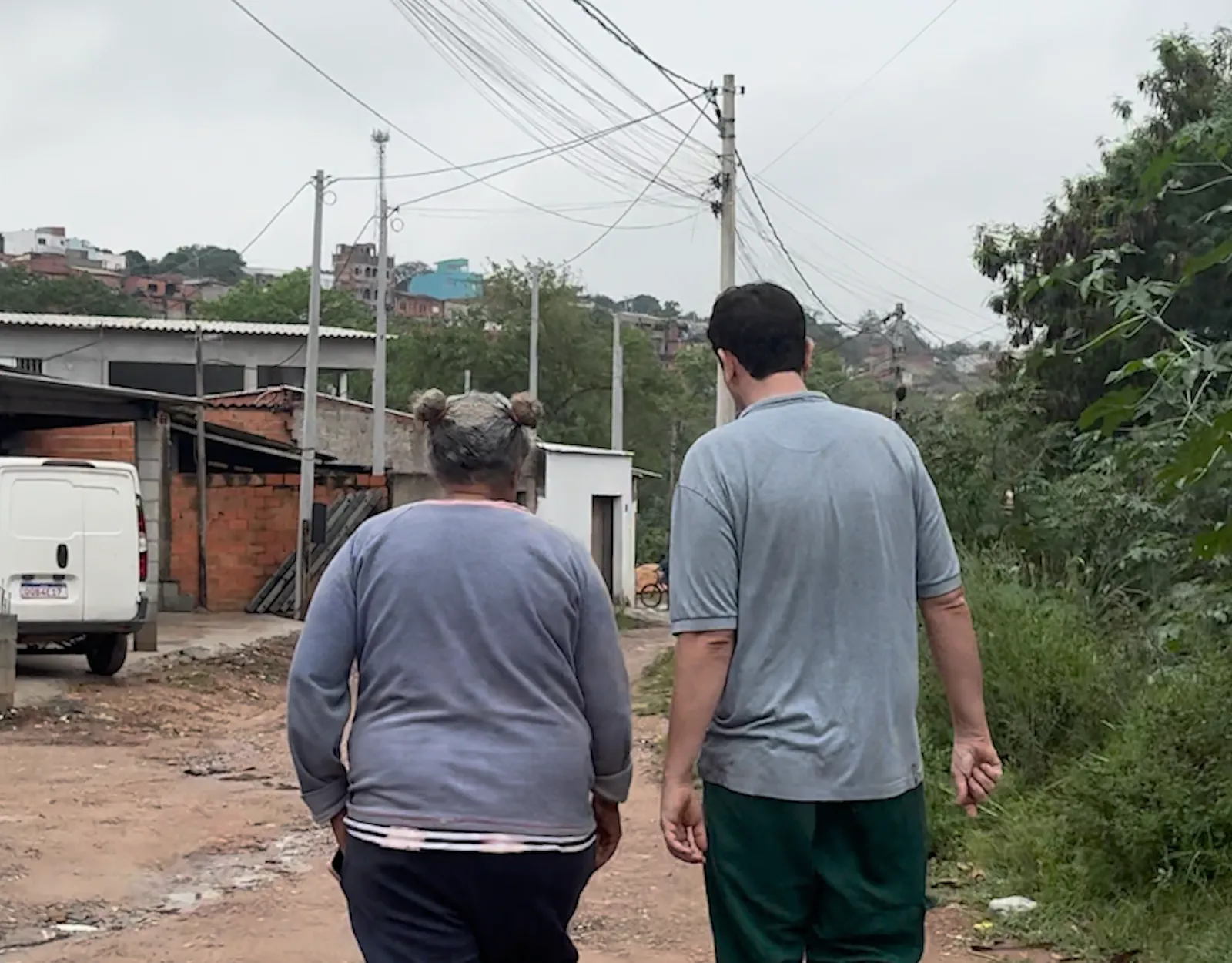 Luzia e Caio de costas, andando pela rua de terra em direção ao lixão